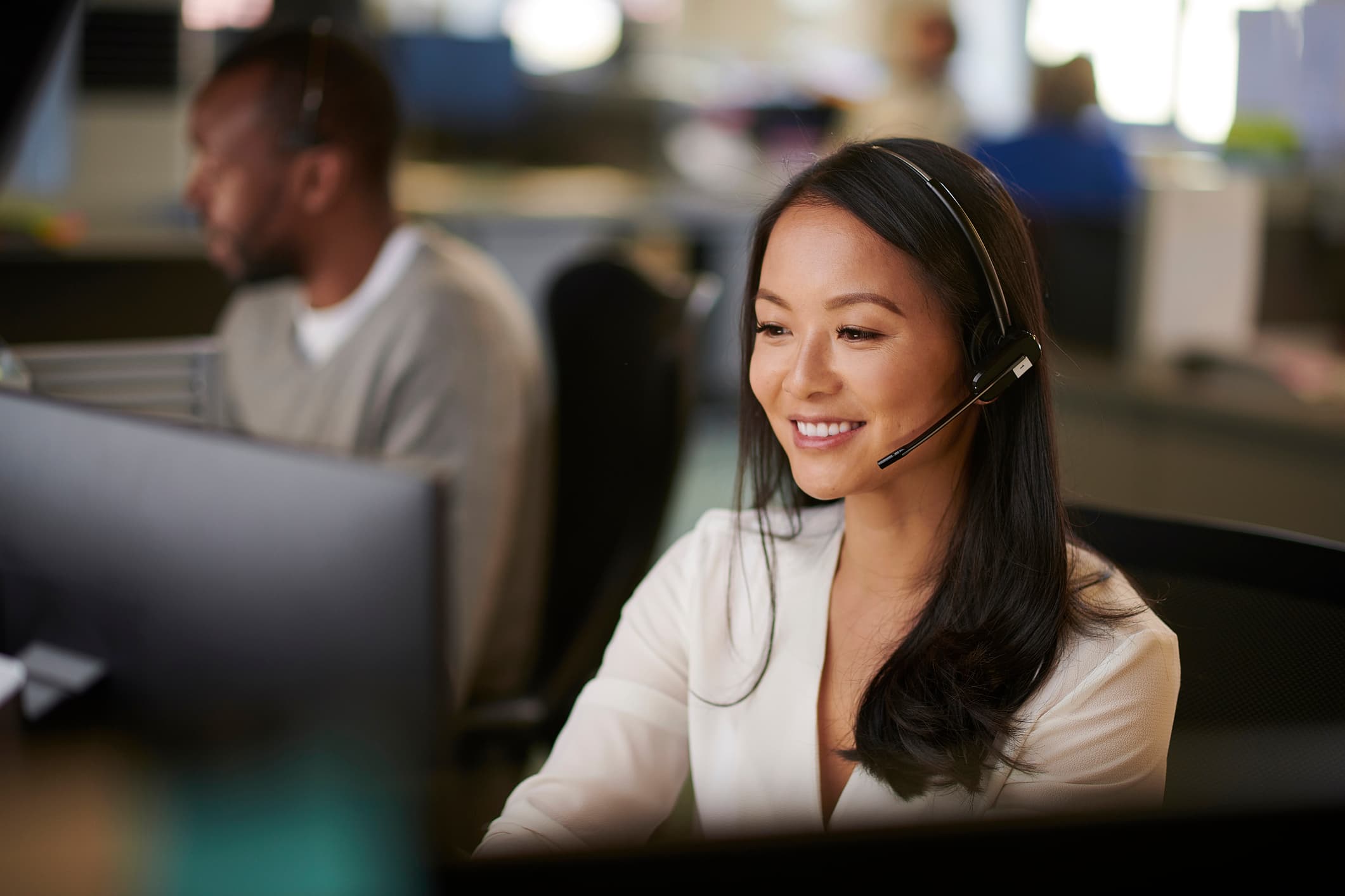A smiling help‑desk technician wearing a headset at a computer workstation, delivering managed IT services in a modern support center.