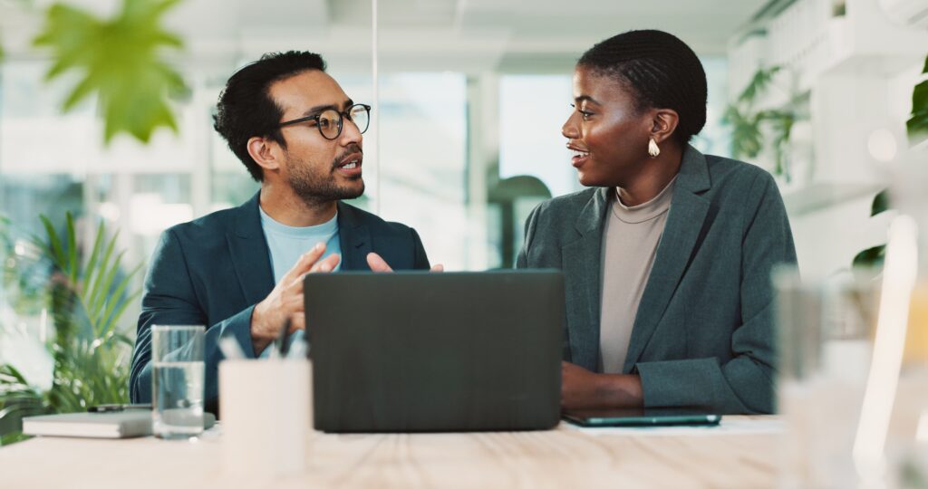 Two business professionals discussing managed unified communications while working on a laptop in a modern office setting