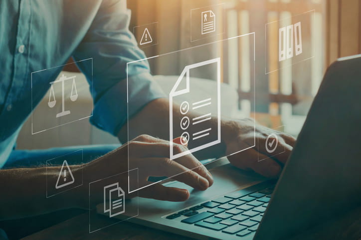 Business professional working on laptop with digital icons of documents and checkmarks symbolizing a compliance checklist